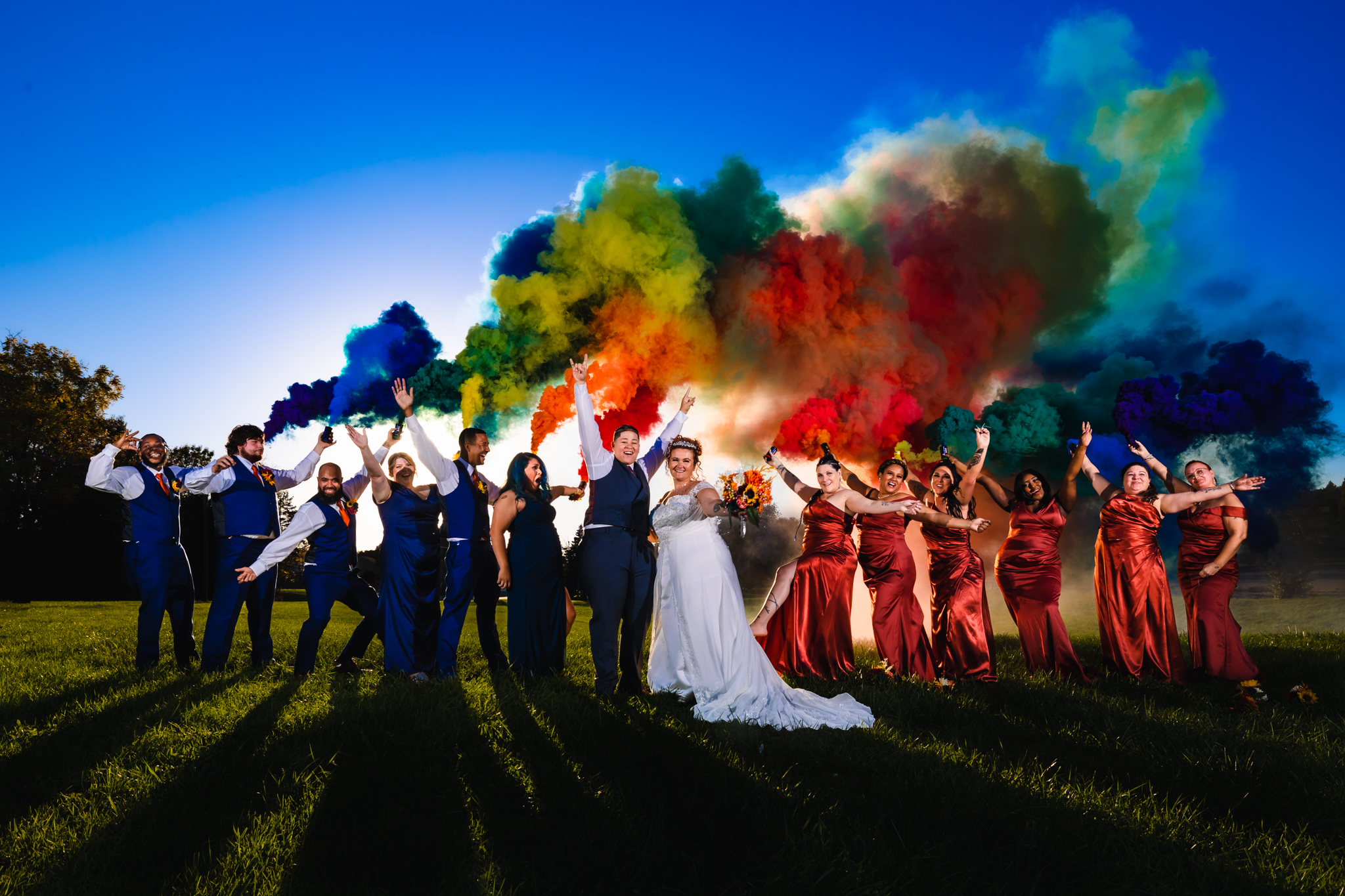 Lesbian couple celebrating their marriage with wedding party as rainbow smoke effects fill the background