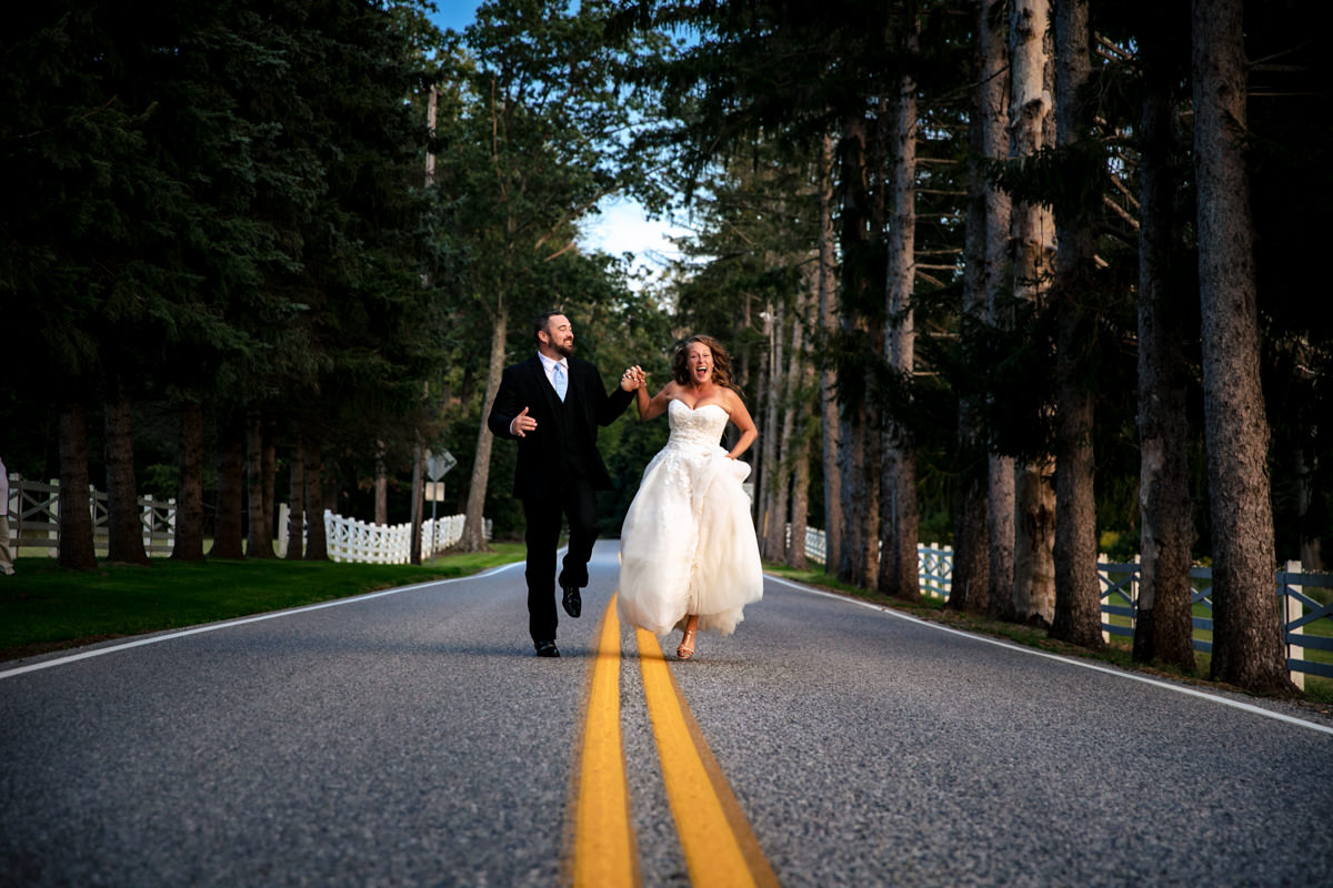 Couple skipping down pine tree lined road toward the camera having the time of their lives