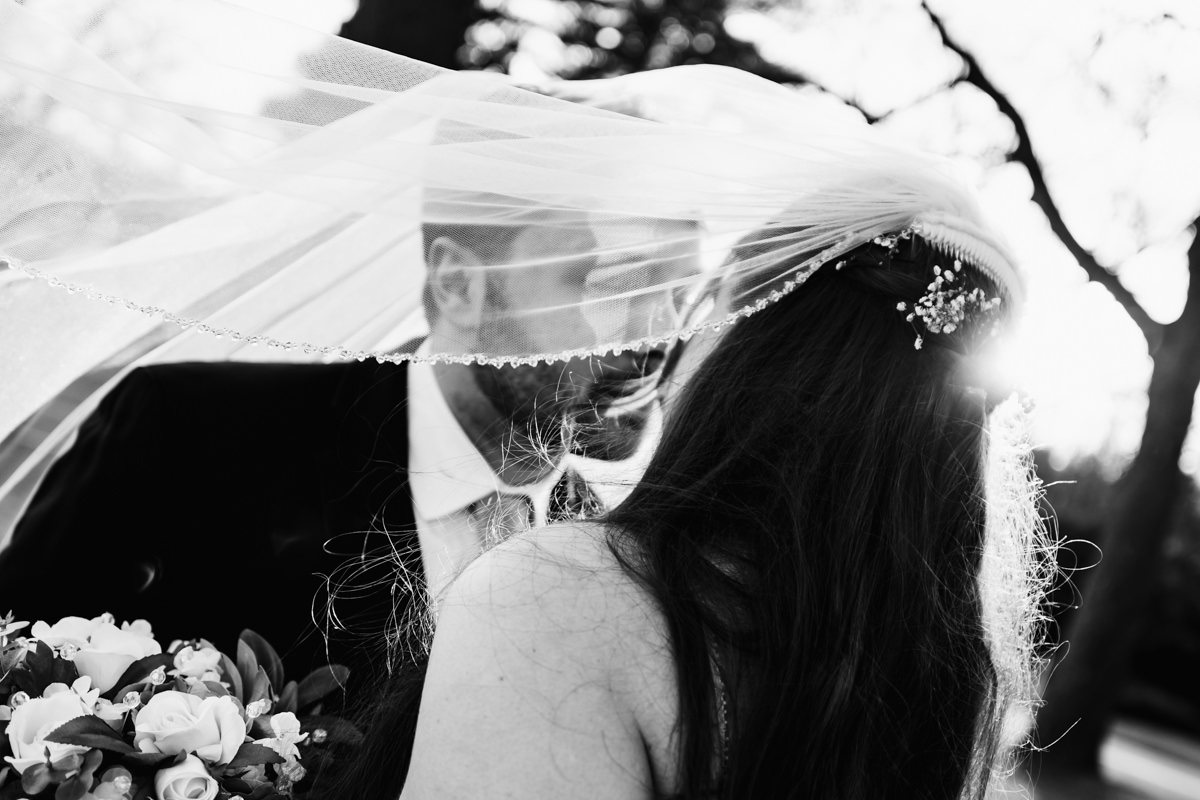 Black and white image of couple kissing under the bride's veil