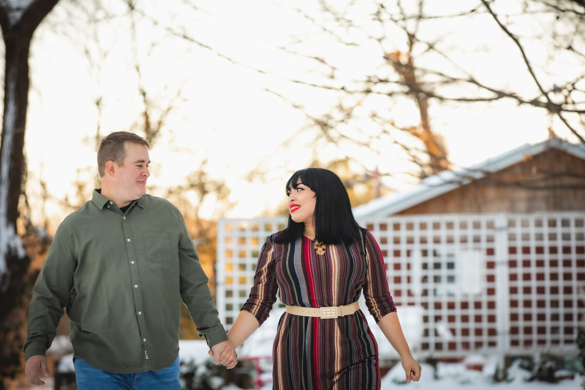 Couple walking through snowy yard during in-home engagement photos
