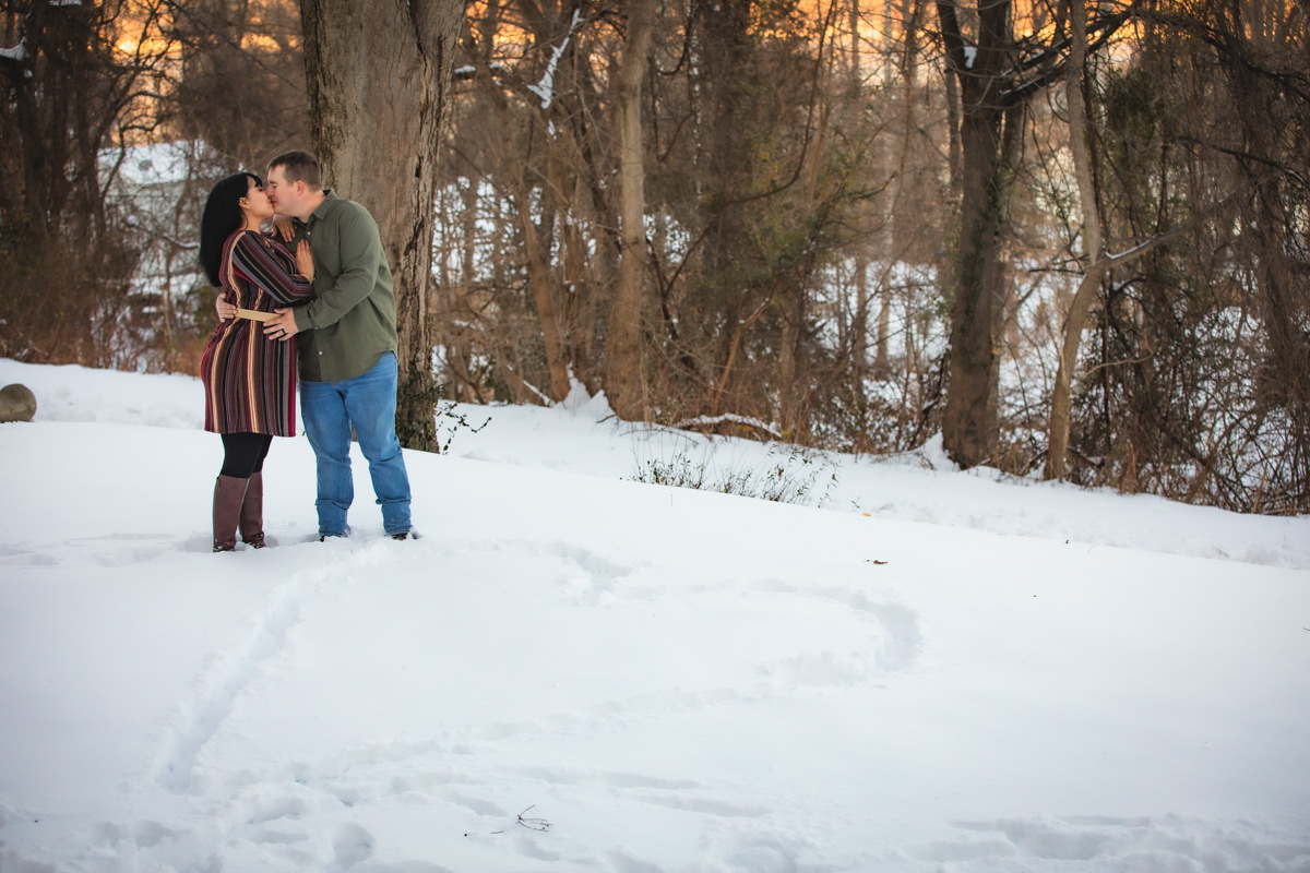 Couple kissing with heart drawn in snow for cozy in-home engagement photos