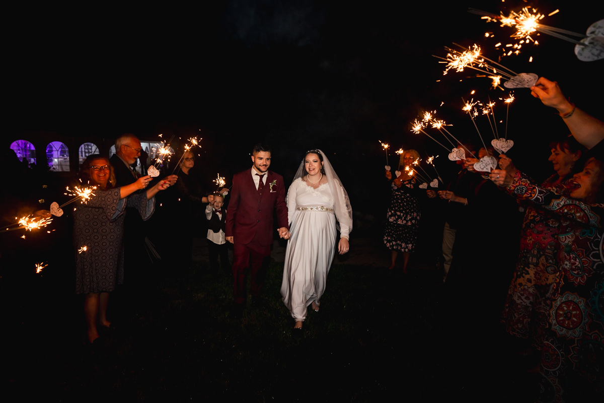 Wedding couple walks through sparkler exit with family