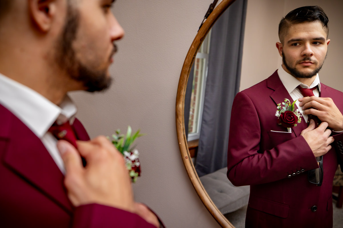 groom straightening crimson tie while getting ready