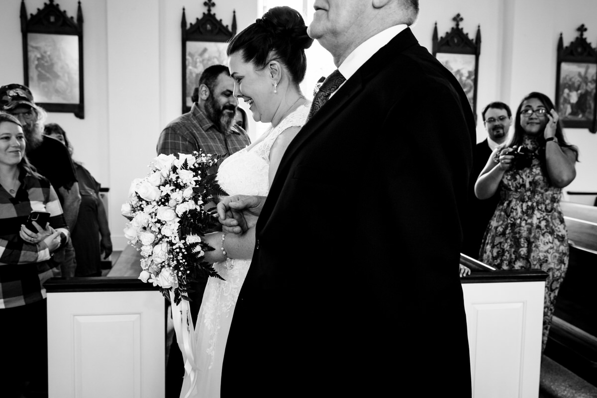 Side angle of bride smiling as her father walks her down the aisle