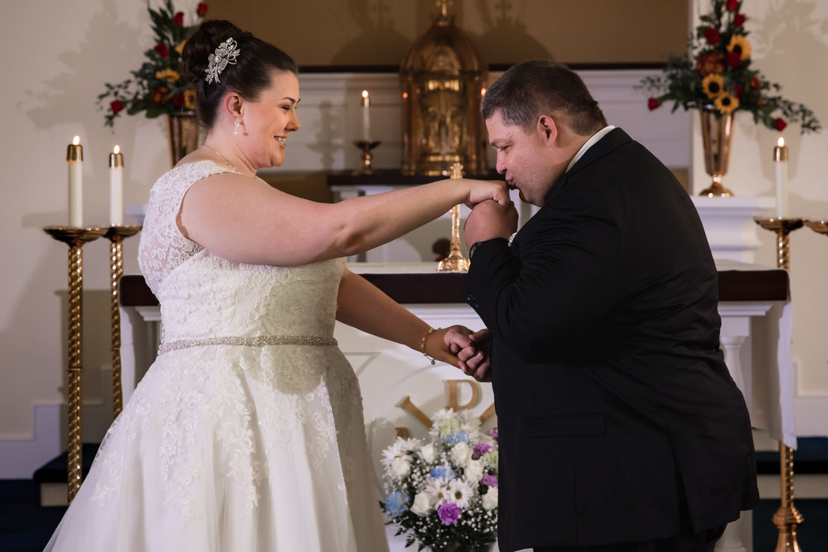 Groom romantically kisses his brides hand at the church alter