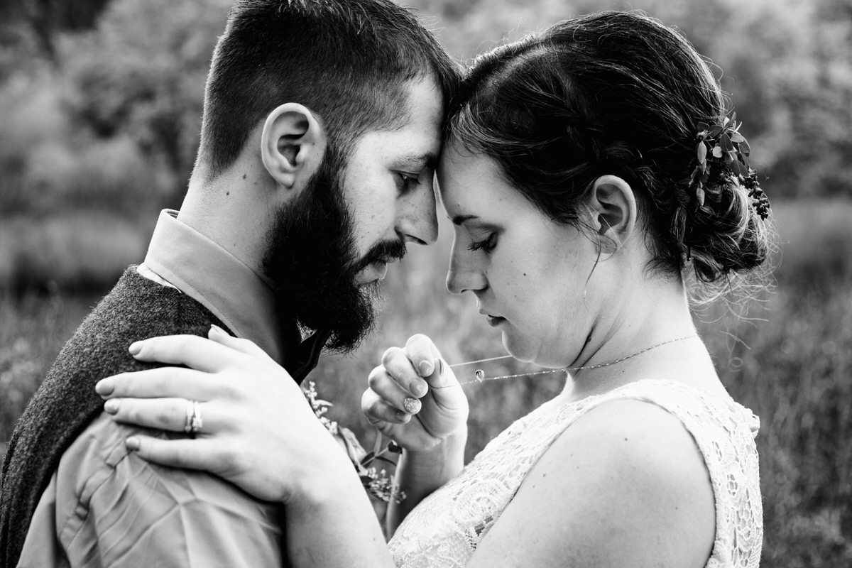Couple leaning foreheads together as bride fixes her necklace during stress-free wedding photos