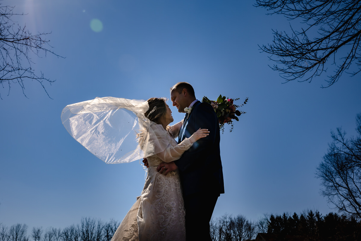 Couple silhouetted on skyline, looking at each other while her veil blows in the wind.