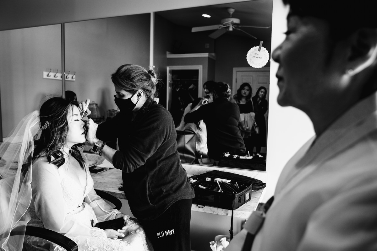 Bride getting makeup done in the bridal suite while proud mother watches