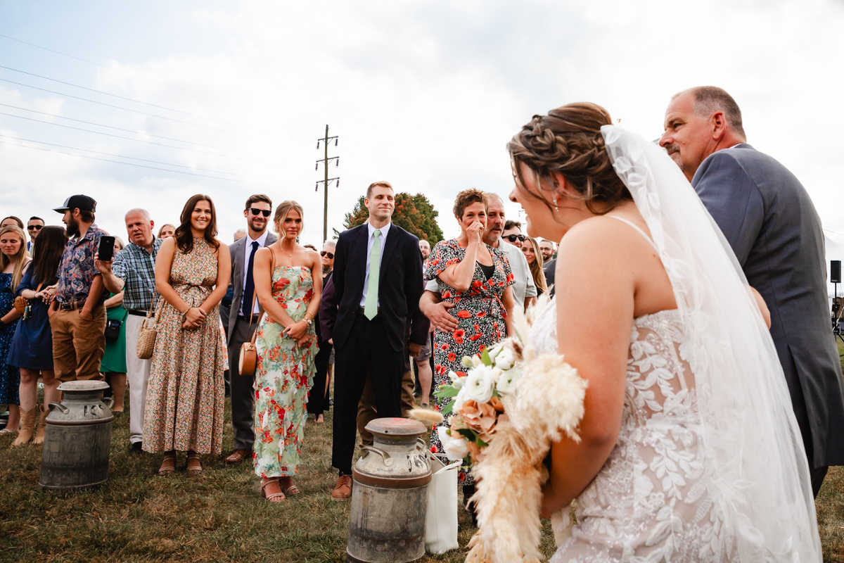 Emotional guest reactions as the bride's father walks her down the aisle on the farm