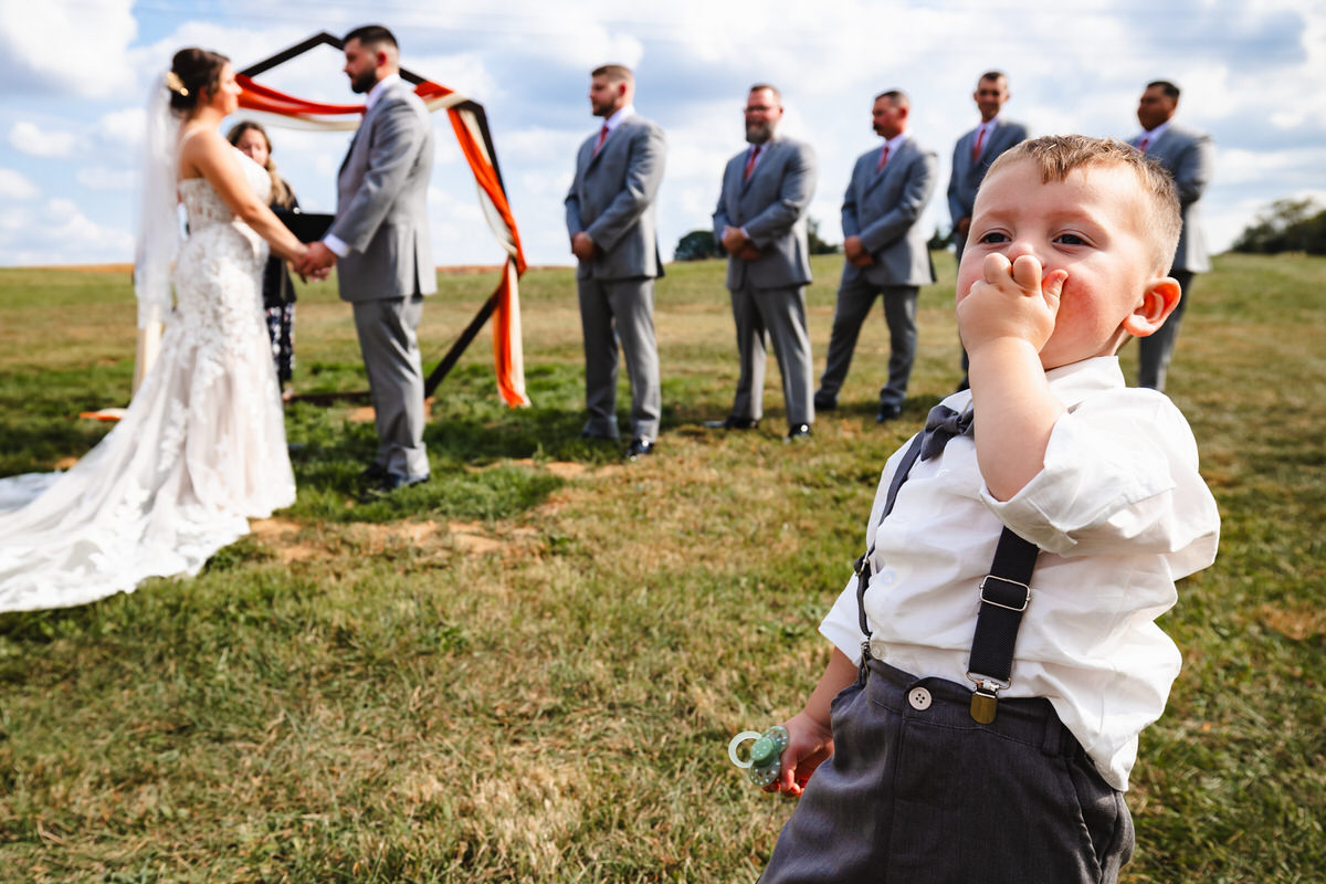 Ring bearer eating snacks in the foreground while couple is saying their vows in background of image