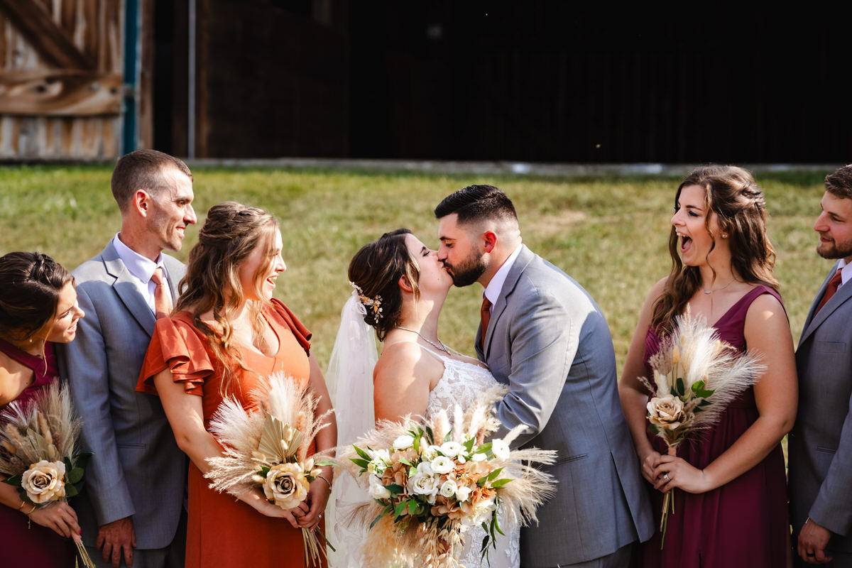 Couple kissing while wedding party looks on in excitement