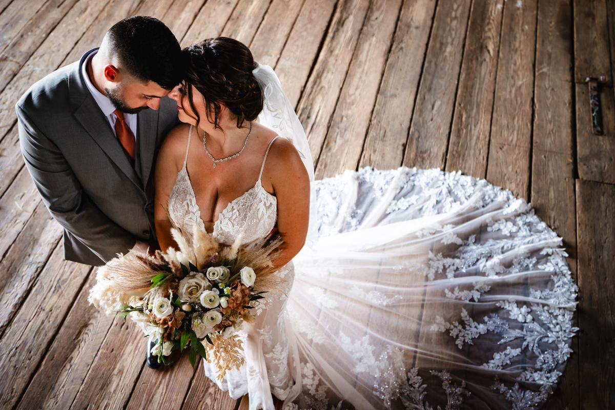 Wood floor barn beams frame the bride and groom as they stand with foreheads together