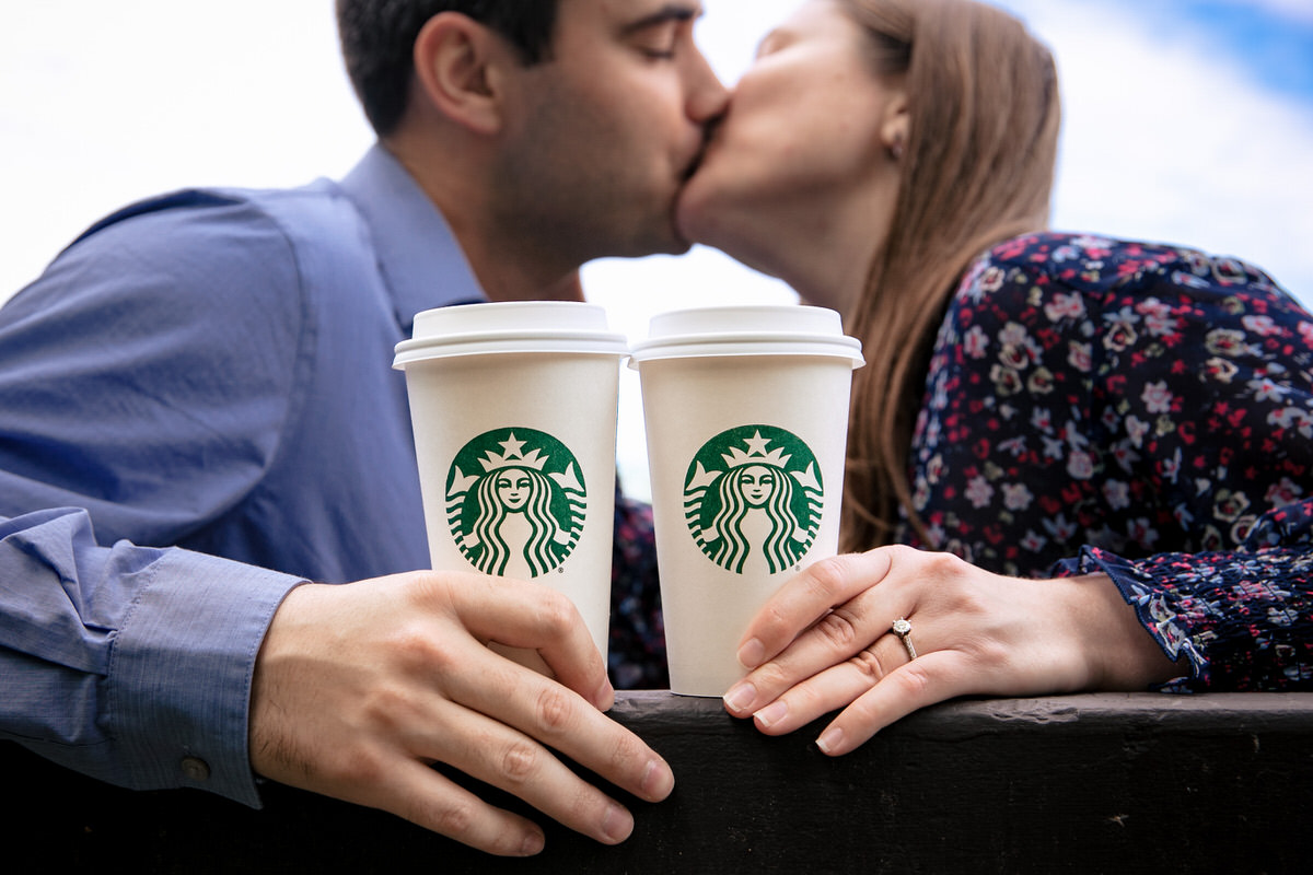Starbucks coffee cups in the foreground of the image while Mariah and Chris kiss in the background.