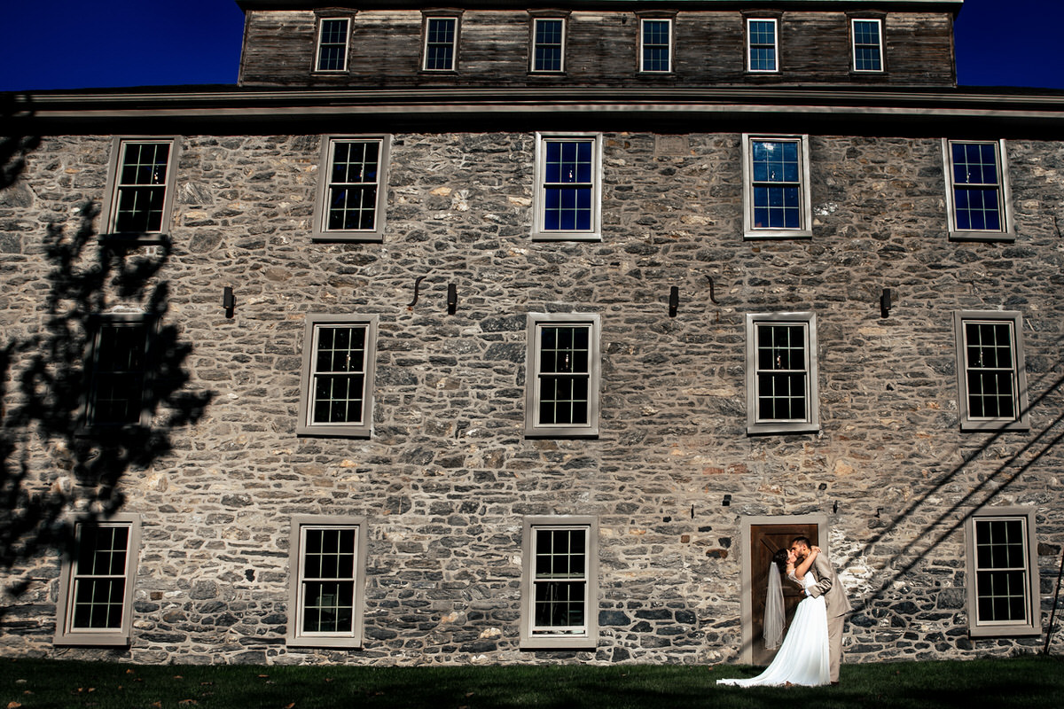 Couple kissing in front of The Mill at Manor Falls.