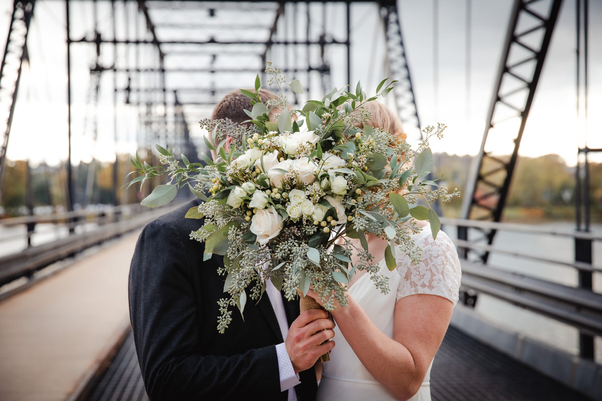 Shy couple kissing behind wedding bouquet.