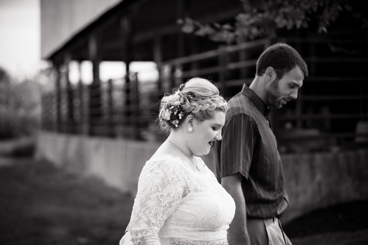 Black and white image of couple walking past barn, hand in hand.